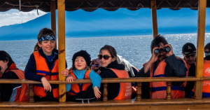 A happy family with children wearing orange life jackets and using binoculars during a safe, scenic boat cruise on Lake Kerkini, Greece.