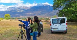Tourists using a spotting scope to observe wildlife with a comfortable tour van and mountain backdrop during our guided day trip to Greece.